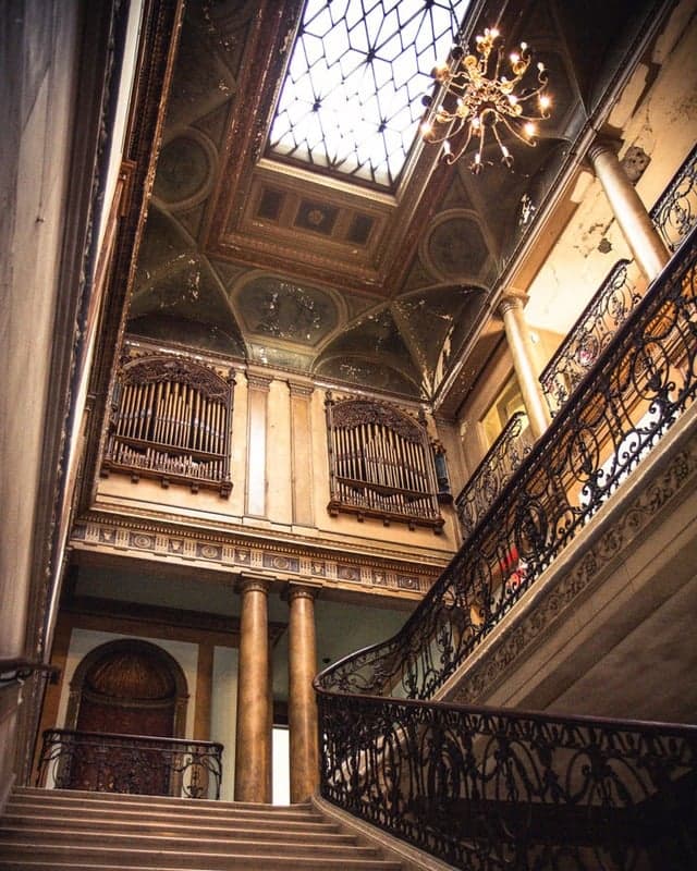 Grand staircase at Alder Manor rising to organ pipe screens and a painted ceiling with a glass skylight