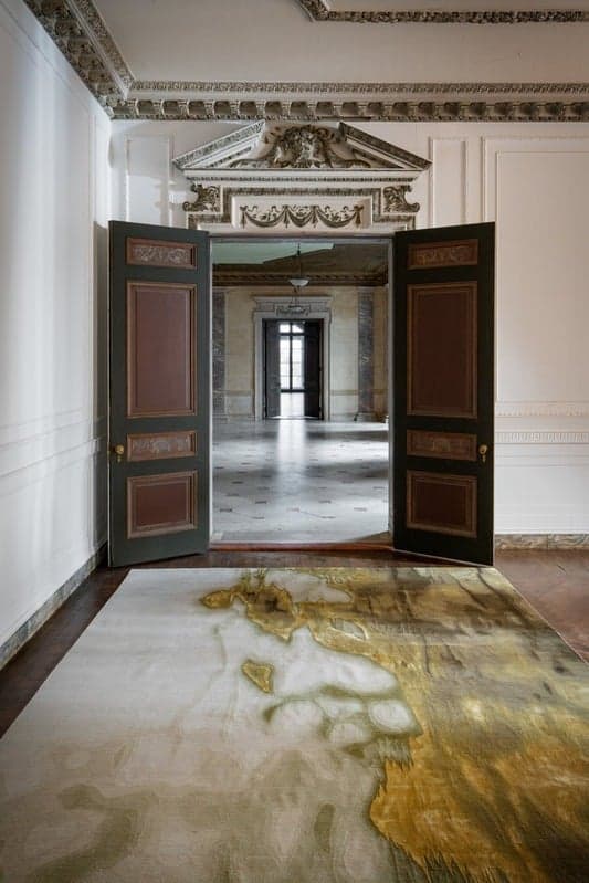 Double doors open from a white paneled room onto a marble hall at Alder Manor, with a gold abstract rug