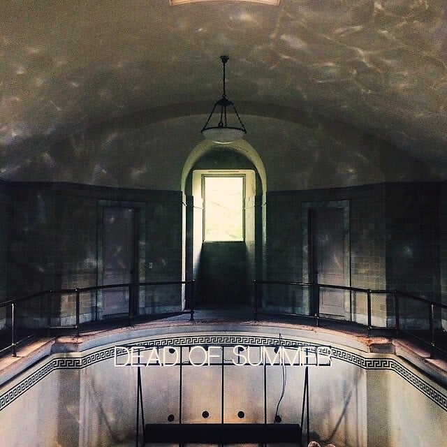 The empty indoor pool at Alder Manor under a vaulted ceiling, lit by a neon sign